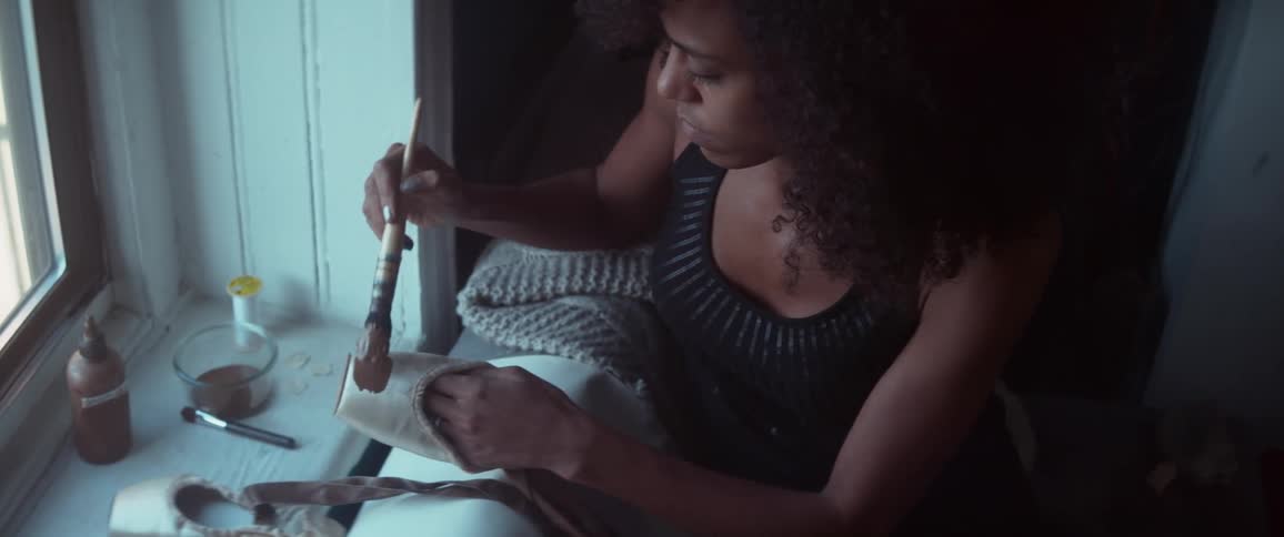 A woman dipping a brush into a bowl of paint before applying the paint to a ballet slipper