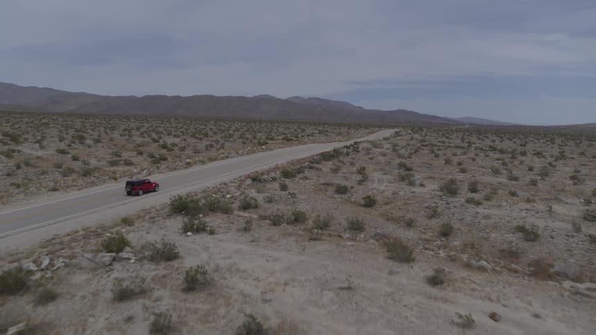 Red vehicle drives along road through desert with mountain on the horizon