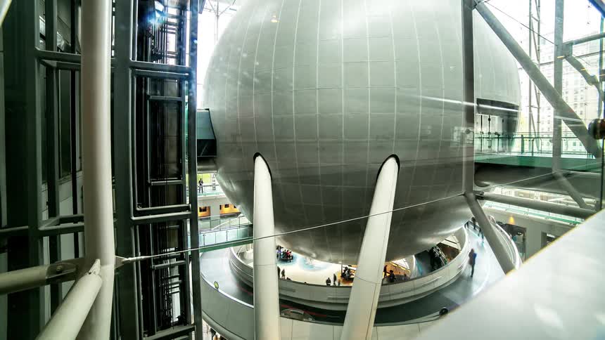 People mill about under a giant steel ball