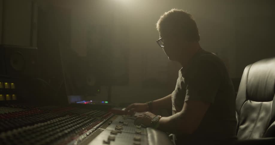 A man sits at a soundboard and makes some adjustments to it