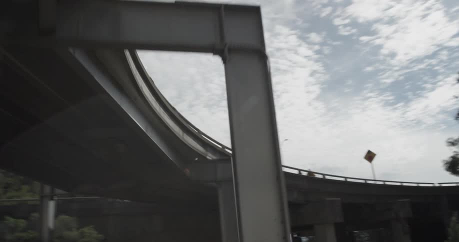 Car drives under a bridge overpass with tress blue skies and clouds on a sunny day