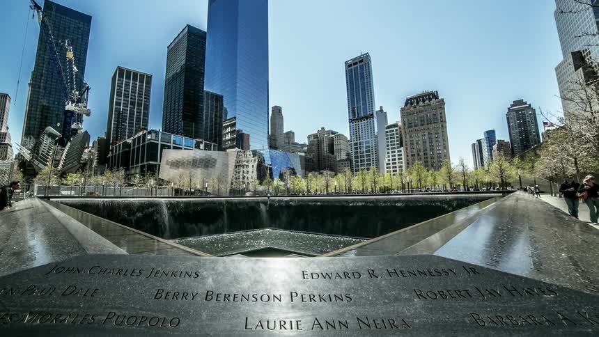 A plaque with names attached to a water fountain in front of a city landscape