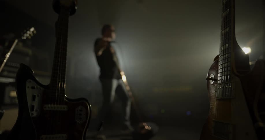 Man holds microphone stand and sings into it in dark room with white light