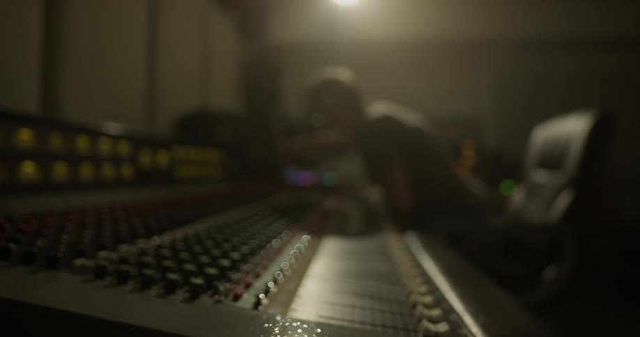 Man  leans forward over audio mixer as he adjusts settings