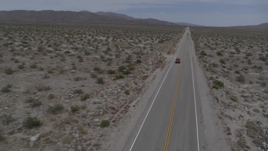 A red jeep can be seen on the road in a desert landscape on a bright sunny day