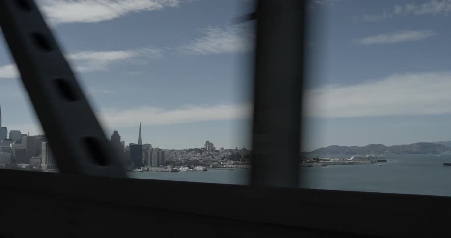 A city appears on the other side of a bridge under a cloudy blue sky