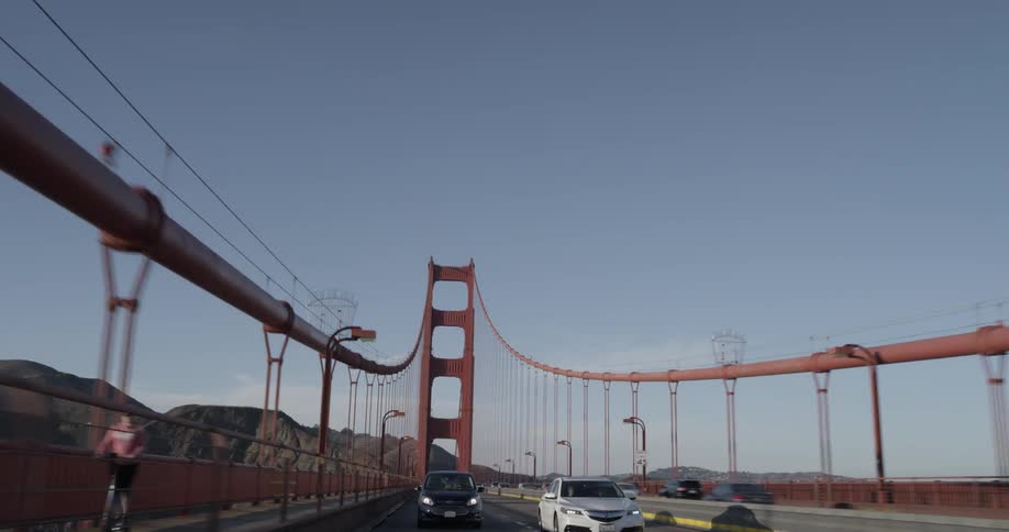 Cars drive across a suspension bridge under a clear blue sky