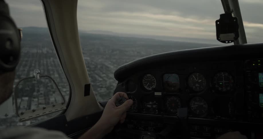 Man flying airplane above city speaks into headset