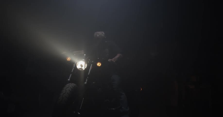 A man walks up to a motorcycle and gets on to roll it forward