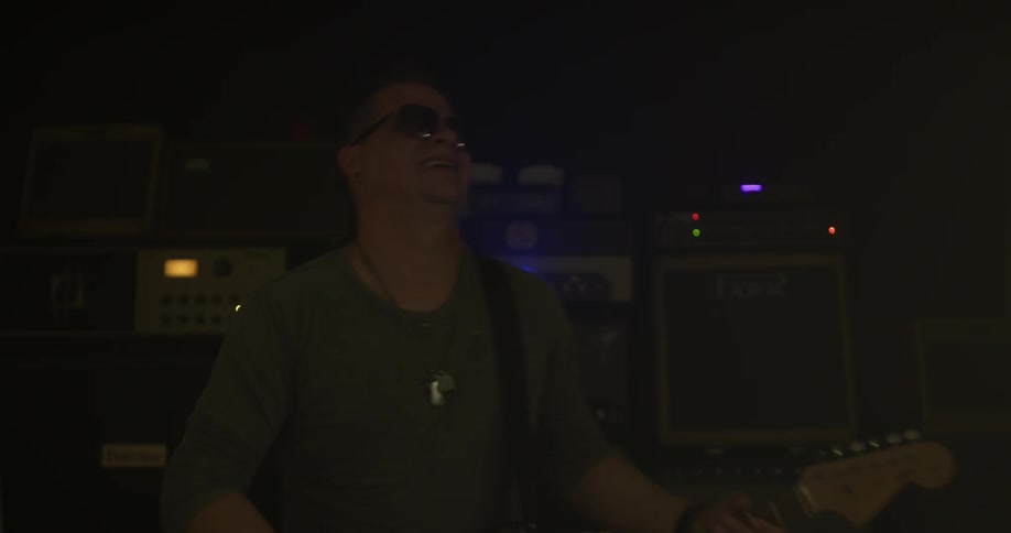 A man plays guitar in a dark room with flashing lights