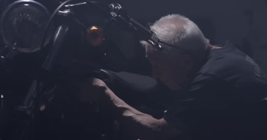 An old man works on a motorcycle in a garage