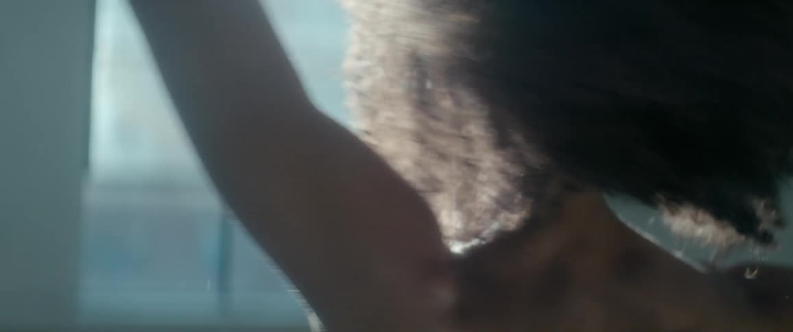 A woman smiles and twirls in the sunlight coming through the windows of a dance studio