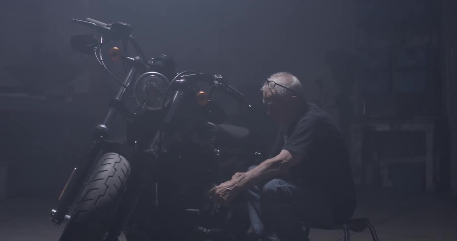An elderly man uses a ratchet on a motorcycle