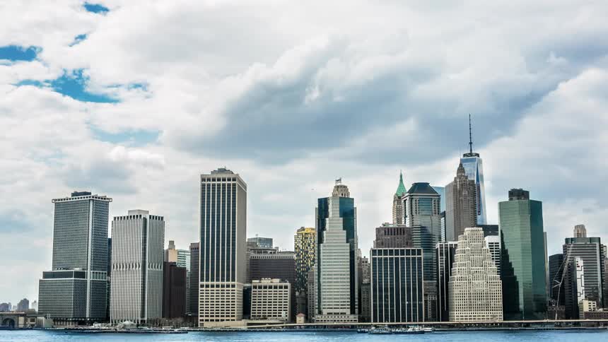Clouds roll by in a time lapse of a city skyline on a blue sky sunny day with a river and boats passing by as well