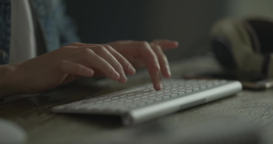 Women wearing a blue jean jacket sits at the computer desk and types on a wireless keyboard for a mac