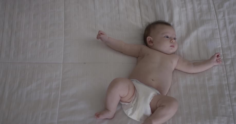 Baby in diaper lying on their back on the bed