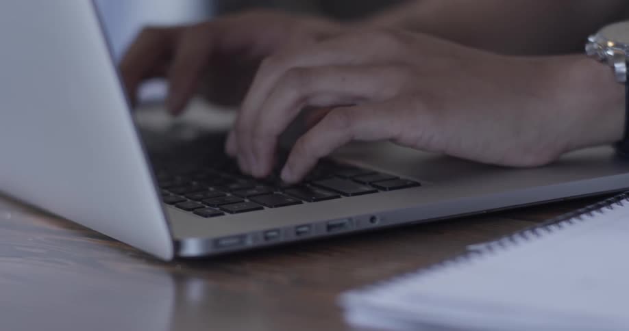 Hands typing on a laptop next to a notebook