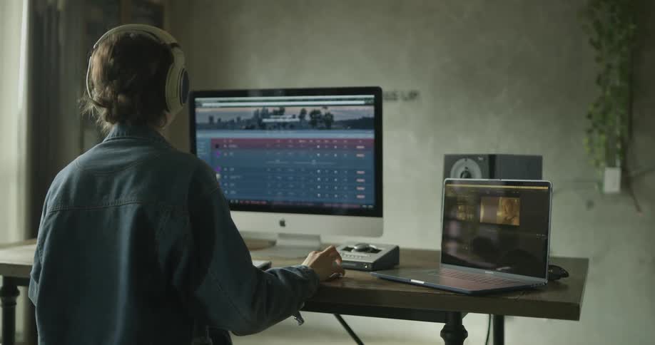 A woman is looking at a computer and putting headphones on