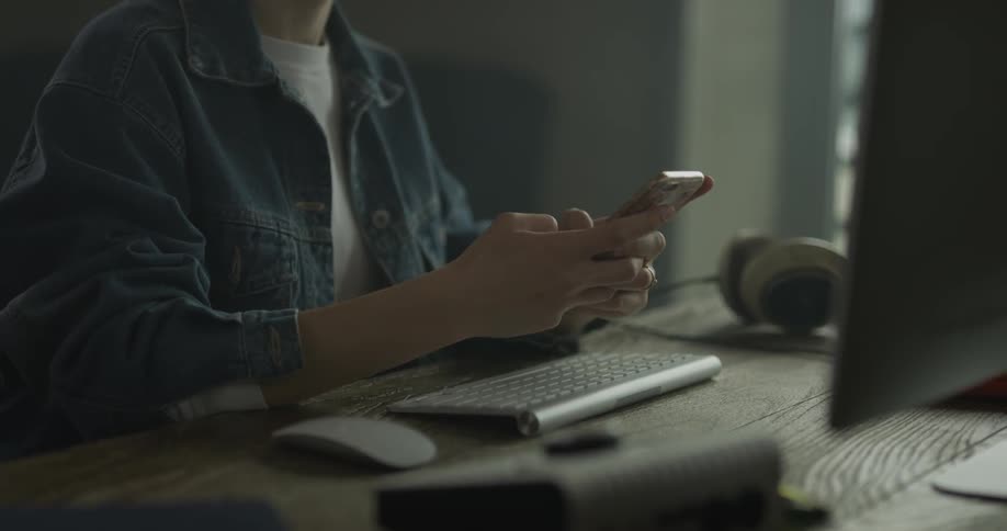 Woman texts on phone while sitting before computer on a desk