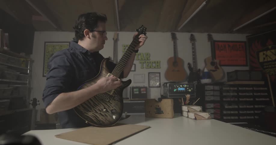 Man in guitar store puts guitar on table then picks it up and plays it