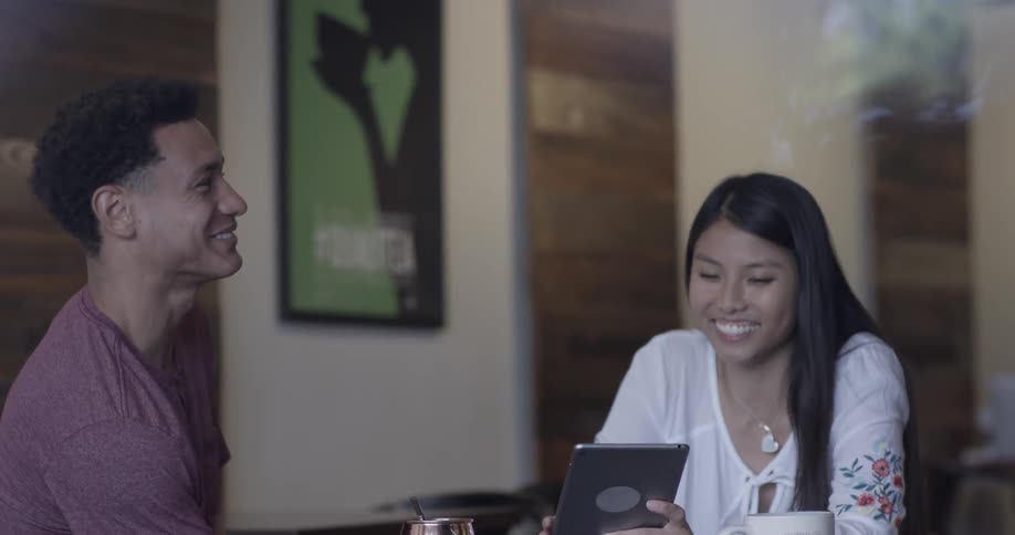 A man and a woman sit at a table and look at something on a tablet screen