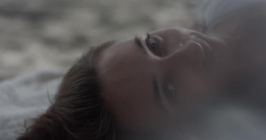 A woman laying in the sand looks around and smiles