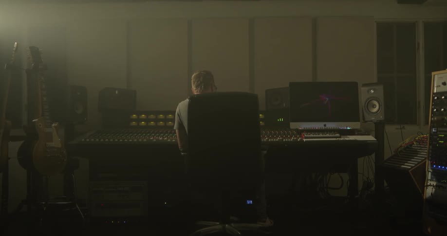 A man sits and works with music equipment
