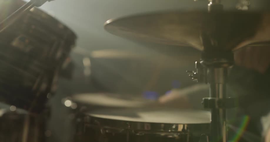 A man plays drums in a dark room with a bright light shining on him