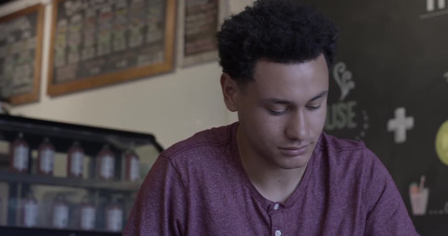 A man writes at a counter and then looks up and acknowledges someone
