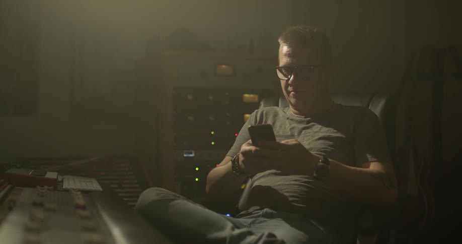 A man types on his phone in front of a mixing board