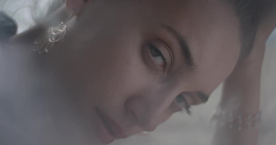 Tight shot of woman's face with gold earrings looking at the camera and wiping the side of her face