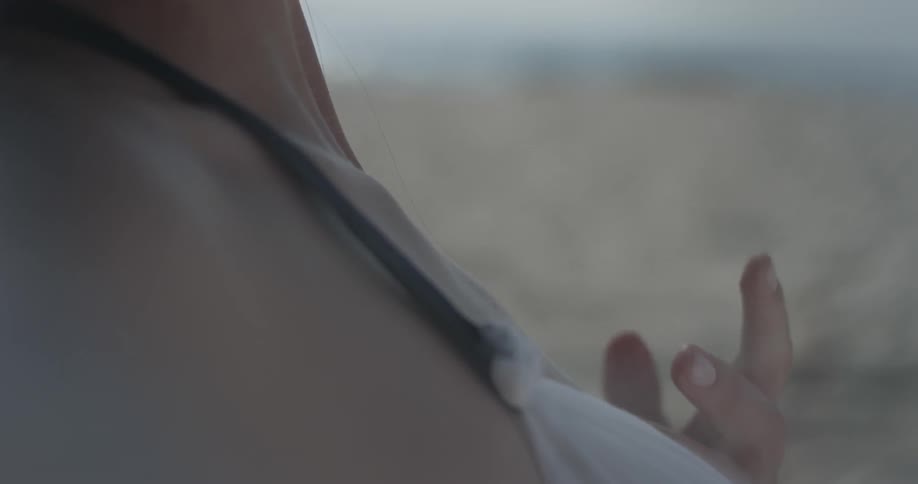 Woman drags a finger down her body while sitting on the beach