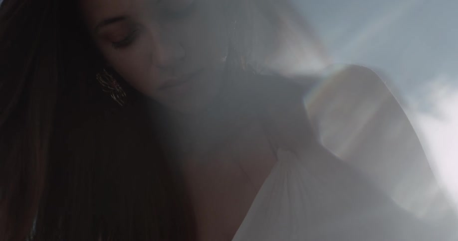 Beautiful pretty women with a thin white dress on and long brown hair is seen in front of the sun beams and lens flares