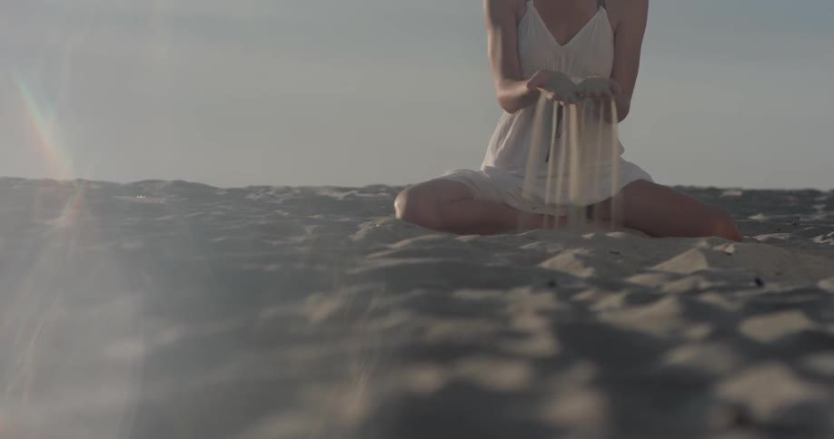 A woman picks up sand and drops it on the beach