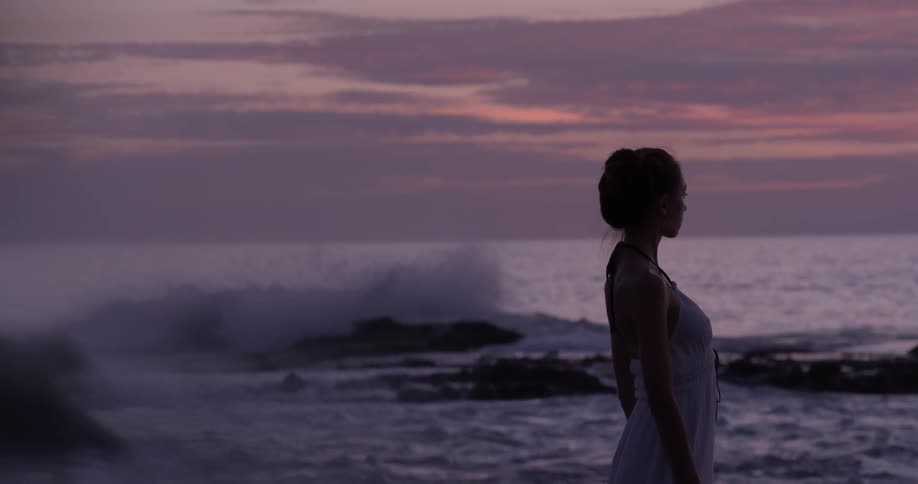 Woman stares into the setting sun across the ocean