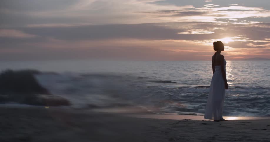 Woman stands on beach at sunset