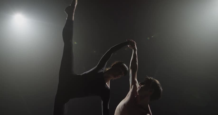 Man braces woman as she stretches one leg upward while they dance