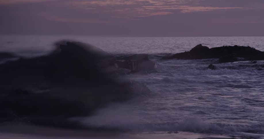 Waves crash among rocks at the beach at dusk