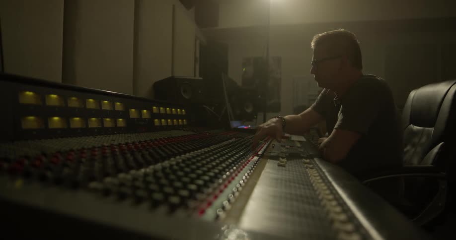 A man sitting in front of a large amount of audio and video controls