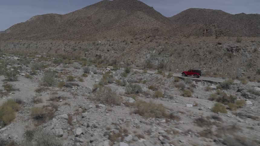 A red jeep drives down a dirt road in the desert