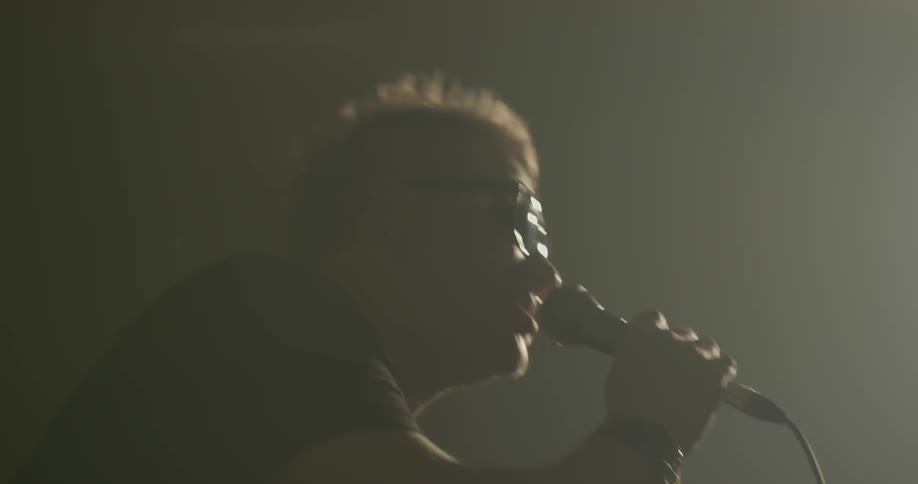 Man holds microphone and its stand as he sings into it