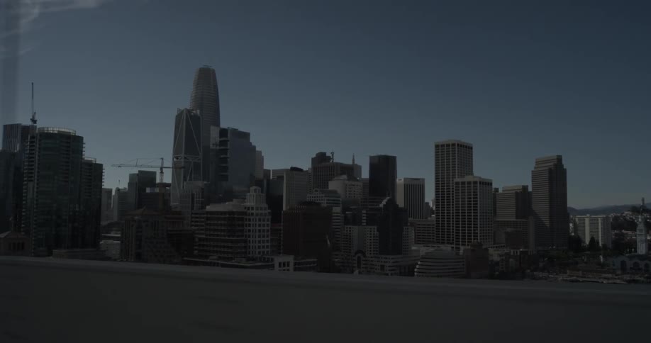 A large major metropolis cityscape can be seen off the side of a bridge the car is driving on and looking over