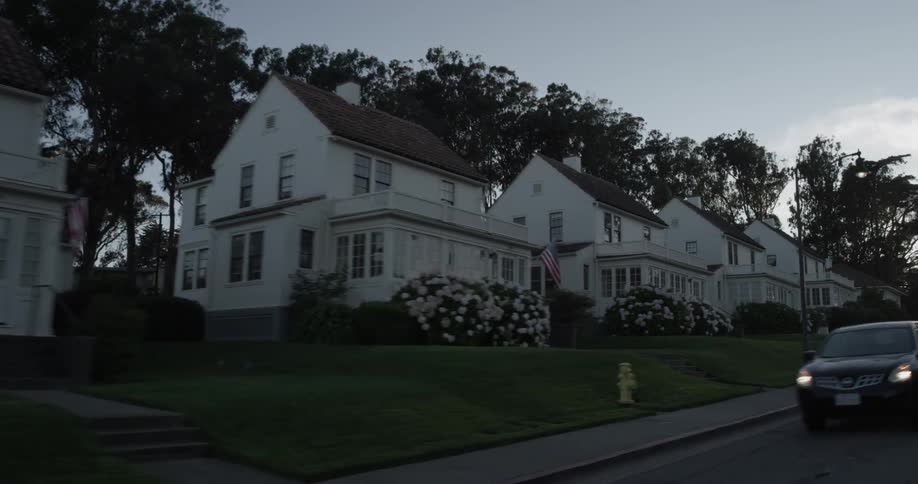 Car drives along road past a row of identical homes