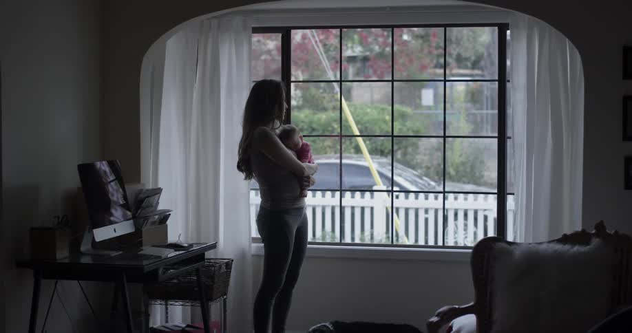 A woman holds a baby in front of a window