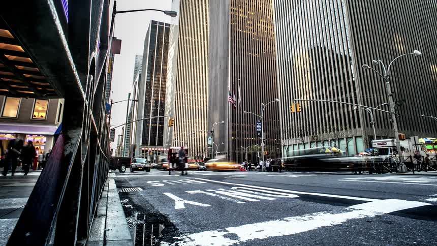 Traffic moves down a city street and pedestrians walk down the sidewalk