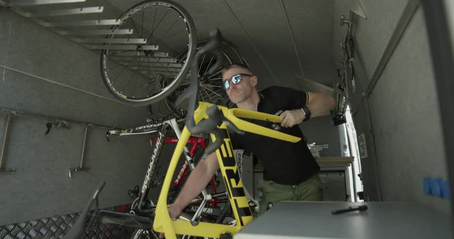 A man lifts a bicycle frame off of a hook