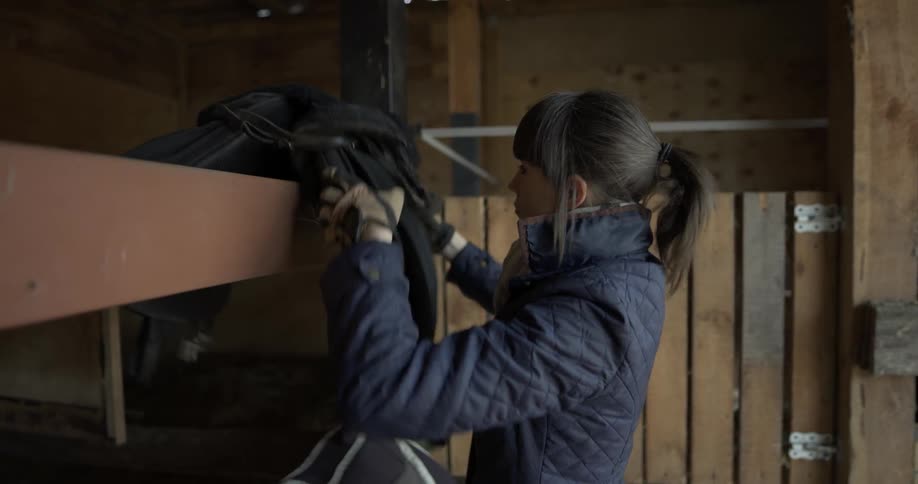 A woman puts a saddle up inside the barn
