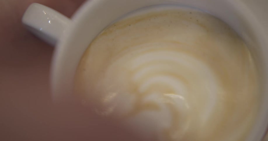 A person's hand is preparing a latte in a cup