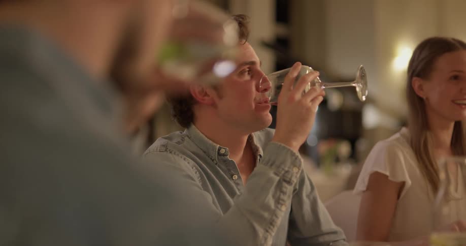 A man laughs and takes a drink from his wine glass during a dinner party with friends