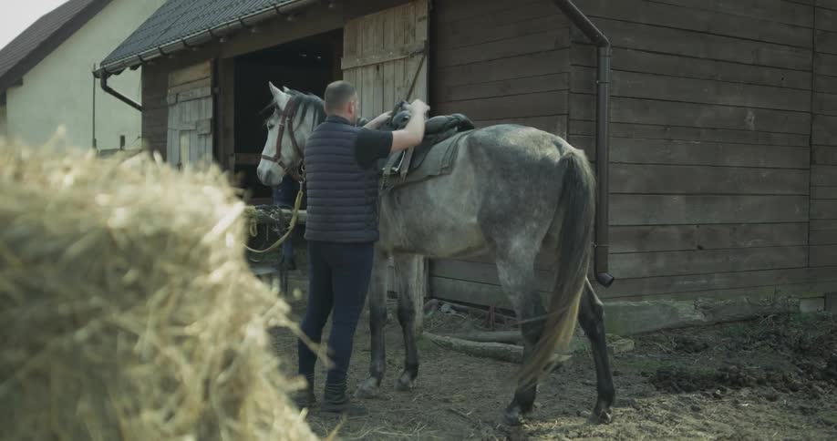 A man places a saddle on a horse